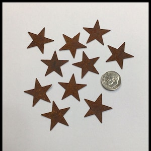 May include: Ten rustic, brown metal stars of various sizes, scattered on a white surface. A US dime is included for scale.