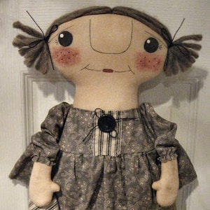 May include: A handmade rag doll with brown hair, a floral print dress, and a striped fabric bag. The doll has a painted face with rosy cheeks and a button nose.