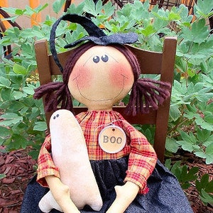 May include: A handmade rag doll dressed in a plaid shirt and denim skirt, holding a white ghost. The doll is wearing a witch hat and has a tag that says "BOO".