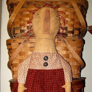 May include: A handmade rag doll with red yarn hair, a red and white plaid skirt, and a floral print top. The doll is standing on top of a stack of wooden baskets.