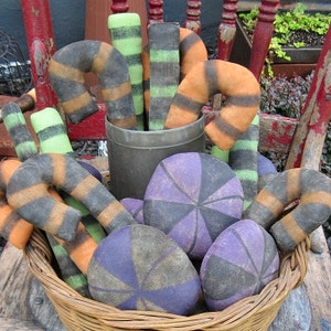 May include: A wicker basket filled with handmade Halloween decorations. The decorations include candy canes with black and orange stripes, and purple and black swirl candy. The basket is sitting on a wooden surface with the text "Chestnut Junction" printed below.
