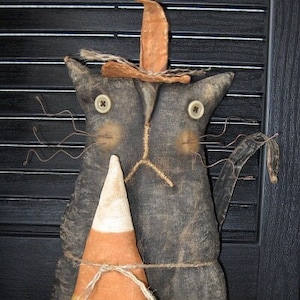 May include: A black cat with a witch's hat and a candy corn prop. The cat is made of fabric and has a stitched face. The candy corn is also made of fabric and has a white, orange, and yellow design.