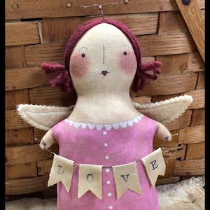 Puede incluir: Muñeca de ángel hecha a mano con un vestido rosa y alas. La muñeca tiene pelo de hilo rojo y un halo. Una pancarta en la parte delantera dice "LOVE". El texto "Chestnut Junction" está en la parte inferior.