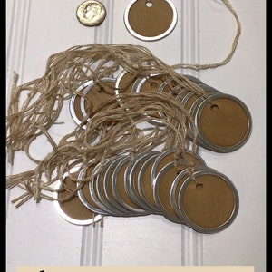 May include: A pile of round, brown paper gift tags with silver metal rims and twine attached. The tags are arranged in a pile with the twine hanging down. The text "Chestnut Junction" is visible at the bottom of the image.