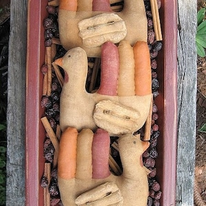 May include: Three handmade fabric turkeys in a wooden tray with cinnamon sticks and dried berries. The turkeys are brown with orange and red feathers.