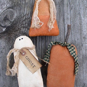 Può includere: Tre decorazioni di Halloween fatte a mano: un fantasma bianco con un'etichetta marrone su cui è scritto "Ghost", un mais dolce arancione e bianco e una zucca arancione con un nastro a quadri verde e bianco.