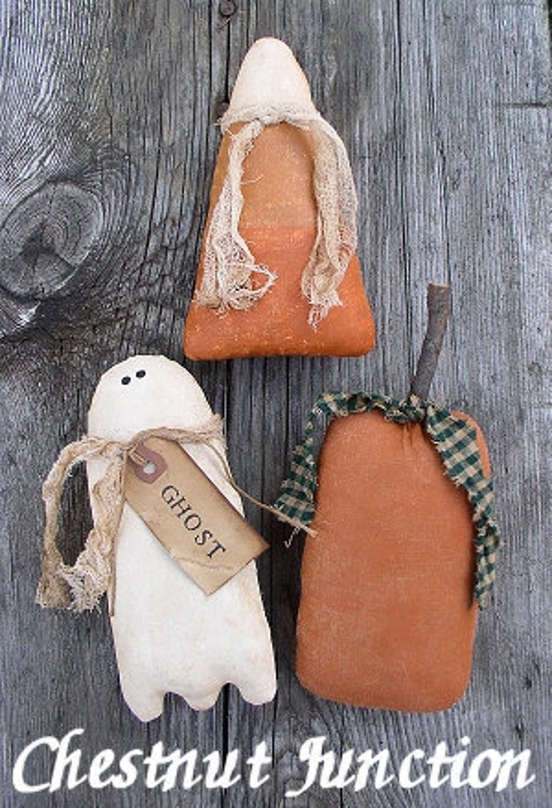 May include: Three handmade Halloween decorations: a white ghost with a brown tag that says "Ghost", an orange and white candy corn, and an orange pumpkin with a green and white plaid ribbon.