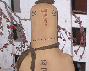 May include: A handmade rag doll snowman with a brown and green striped scarf. The snowman has a stitched-on face with a carrot nose and black eyes. The snowman is standing in front of a white picket fence.