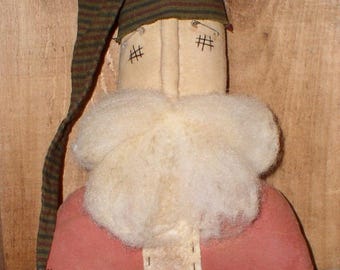 May include: A handmade rag doll Santa Claus with a red and white suit, a white beard, and a striped green and brown hat. The doll has a bell attached to the hat.