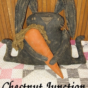 May include: A black fabric bunny rabbit holding a large orange carrot. The bunny is sitting on a white and pink checkered fabric. The text "Chestnut Junction" is printed below the bunny.