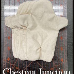 May include: A beige, quilted oven mitt with a curved shape. The mitt is made of a textured fabric and has a folded cuff. The text "Chestnut Junction" is at the bottom of the image.