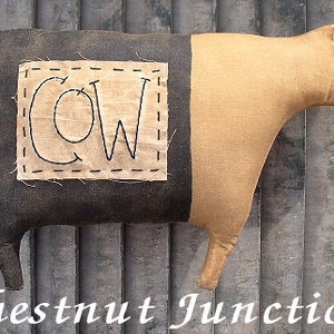 May include: A brown and black fabric cow with a stitched patch on its side that says "COW".