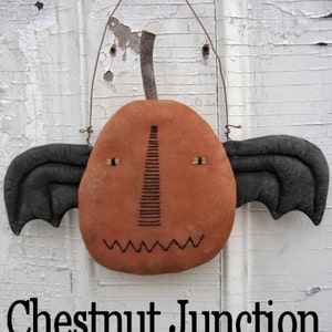 May include: A handmade orange pumpkin with black bat wings and a stitched face. The pumpkin is hanging from a wire loop. The text "Chestnut Junction" is visible below the pumpkin.