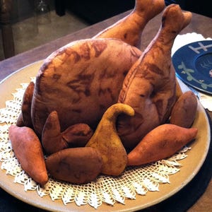 Puede incluir: Un pavo de tela marrón y beige con un encaje blanco sobre un plato marrón. El pavo está hecho de tela y tiene un aspecto realista.