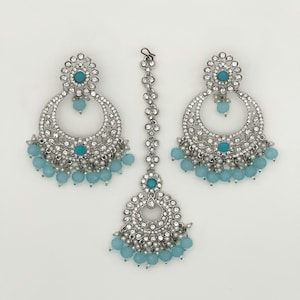 May include: A silver-toned jewelry set featuring a pair of large, ornate earrings and a headpiece. Each piece is embellished with clear crystals and turquoise-colored beads. The earrings and headpiece have a matching design.