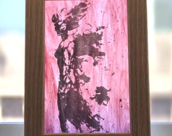 Puede incluir: Un marco de madera rectangular que contiene un panel de vidrio rosa translúcido. El vidrio presenta una silueta oscura y abstracta de una figura con cabello o alas que fluyen, representada en un patrón texturizado similar a la tinta.