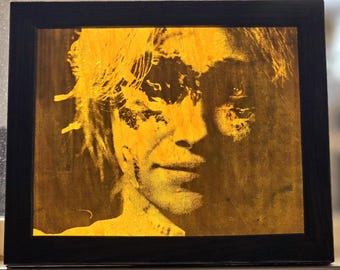 Puede incluir: Una caja de luz rectangular que presenta un retrato en amarillo dorado de alto contraste de una persona con cabello texturizado y en capas. La imagen está dentro de un marco negro simple y sólido, creando un marcado contraste visual entre el sujeto brillante y el borde oscuro.