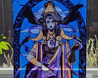 Puede incluir: Una pieza de arte en vidrio rectangular con una ilustración estilizada de una figura de cabello oscuro, que lleva tocado dorado y joyas con gemas azules. La figura se sitúa sobre un fondo azul vibrante con patrones arqueados negros.