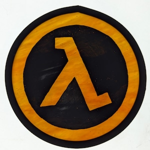 May include: A circular, yellow and black wooden sign with a stylized, yellow Lambda symbol in the center. The symbol is a stylized letter L.