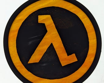 Peut inclure: Un panneau rond en bois jaune et noir avec un symbole Lambda stylisé jaune au centre. Le symbole est une lettre L stylisée.