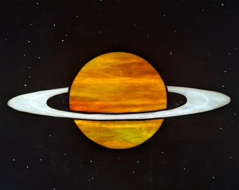 Peut inclure: Une œuvre d'art céleste représentant la planète Saturne sur un fond noir parsemé d'étoiles blanches. La planète est représentée dans des tons de jaune et d'orange, avec un anneau blanc proéminent. L'œuvre évoque l'émerveillement cosmique.