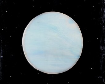 Puede incluir: Un disco circular jaspeado en azul pálido y blanco centrado sobre un fondo negro sólido. El disco presenta sutiles patrones de remolinos en azul claro y blanco que recuerdan a un planeta, mientras que el fondo negro está salpicado de diminutos puntos blancos.