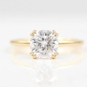 May include: A gold engagement ring with a large, clear, cushion-cut diamond.