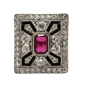 May include: Square-shaped ring with a central rectangular pink gemstone, surrounded by white diamonds and black accents. The ring has a silver-colored metal setting and a detailed, geometric design. The overall style is vintage or Art Deco.