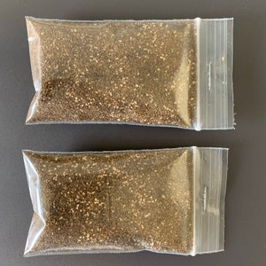 May include: Two clear plastic bags filled with brown and gold colored sand. The bags are sealed with a zipper.