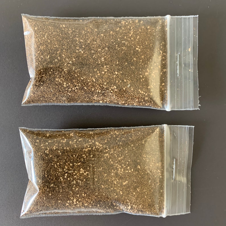 May include: Two clear plastic bags filled with brown and gold colored sand. The bags are sealed with a zipper.
