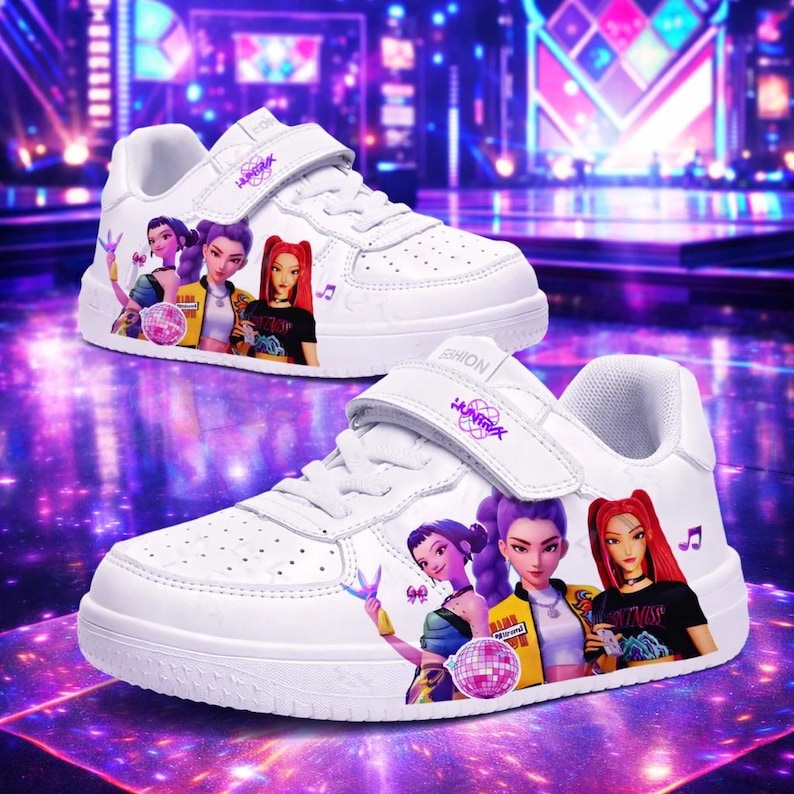 May include: White trainers with a hook-and-loop strap, decorated with a colourful graphic of three animated women. The shoes have a perforated design and the word "HUNTRIA" is printed on the strap.