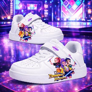 May include: White trainers with a hook-and-loop strap. They feature a colourful graphic of three anime-style characters with weapons. The shoes have the text "K Demon Hunters" and "Fashion" printed on them.