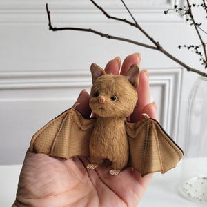 May include: A brown plush bat with large, brown fabric wings. The bat has a small, pink nose and black eyes.