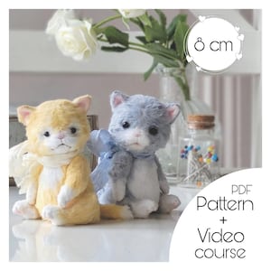 May include: Two handmade plush cat toys, one yellow and one gray, with white accents. They are sitting on a white surface. The text "PDF Pattern + Video Course" is in the bottom right corner of the image. The text "8 cm" is in a circle in the top right corner of the image.