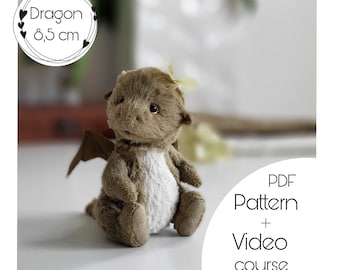 May include: A brown plush dragon toy with a white belly, sitting on a white surface. The dragon is 8.5 cm tall. The image includes the text "Dragon 8,5 cm" and "PDF Pattern + Video course".