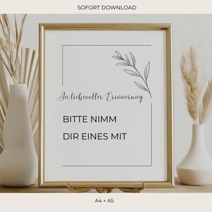 Könnte beinhalten: Ein gerahmter Druck mit goldenem Rahmen, der den Text "In liebevoller Erinnerung" und "Bitte nimm dir eines mit" zeigt. Eine zarte botanische Illustration schmückt die obere rechte Ecke. Der Druck steht auf einer Holzoberfläche mit dekorativen Vasen.