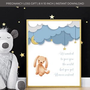 May include: A framed print with a gold border features a watercolor illustration. A tan bunny sits below blue clouds, a crescent moon, and stars. The text reads, "We wanted to give you the world but you got Heaven instead."