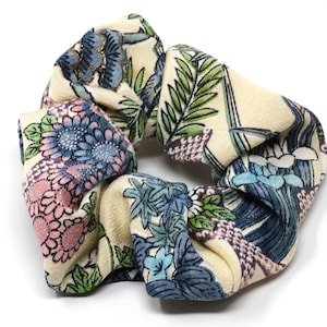 Könnte beinhalten: Ein floral gemusterter Haargummi mit cremefarbenem Hintergrund und floralen Designs in Blau, Rosa und Grün. Das Haaraccessoire besteht aus einem weichen Material und ist zum Zusammenhalten der Haare gedacht.
