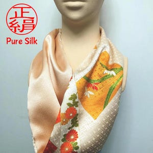 Peut inclure: Un foulard en soie beige avec un motif floral dans des tons d'orange, de jaune et de vert. Le foulard est plié en forme de triangle et porté autour du cou. Le texte "Pure Silk" est imprimé sur le foulard.