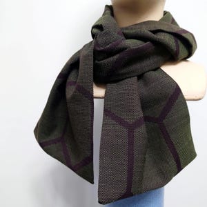 以下が含まれることがあります： 緑と茶色の幾何学模様の入ったスカーフ。スカーフは柔らかく織られた生地で作られています。