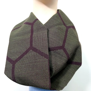 Może przedstawiać: Zielono-fioletowy szal z tkaniny z geometrycznym wzorem. Szal jest złożony na pół i ma dekolt w kształcie litery V.