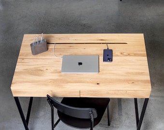 Könnte beinhalten: Ein heller Schreibtisch aus Holz mit rechteckiger Platte, zwei Schubladen an der Vorderseite und schwarzen Metallbeinen. Ein silberner Laptop, ein dunkles Smartphone und ein grauer Stiftehalter stehen auf der Oberfläche. Ein schwarzer Stuhl steht davor.