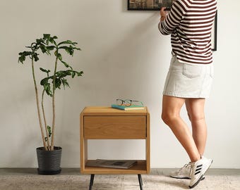 May include: A light oak nightstand with a single drawer and an open lower shelf, supported by four thin black metal legs. The nightstand features rounded corners and a natural wood grain finish, providing a functional storage piece for a bedroom.