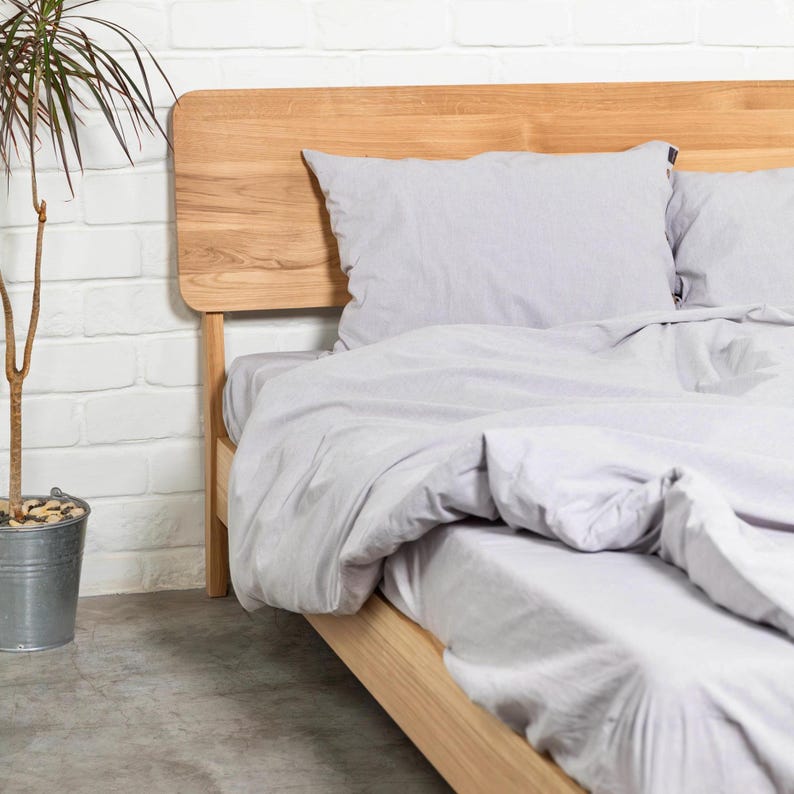 May include: A wooden bed frame with a light gray duvet and two pillows. The headboard is made of solid wood and has a natural finish.