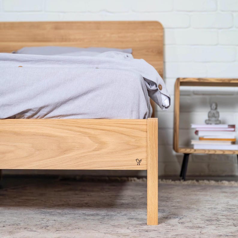 May include: A wooden bed frame with a light gray sheet and a small bird logo on the side. The bed frame is made of solid wood and has a simple design.