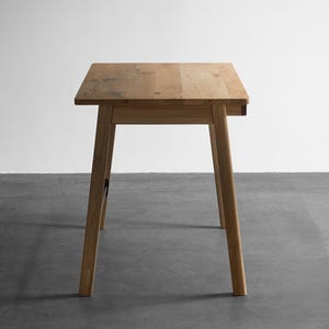 May include: A light brown wooden table with a rectangular top and four tapered legs. The table features a natural wood grain pattern throughout the surface and structure, showcasing a simple, functional design with clean lines and a smooth finish.