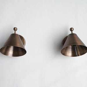 Handcrafted Solid Brass Wall Sconce Pair Featuring Classic Finial Accents and Traditional Decorative Detailing, Shown Together as A Coordinated Set. Each Fixture Has a 7 Inch Width, 8 Inch Height, and 5 Inch Round Canopy with A Warm Vintage Inspired Appearance, Frost Lights.