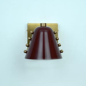 This Handcrafted Wall Light Pairs a Rich Wine Cone Shade with Warm Brass Detailing, Showing a Clean Silhouette and Carefully Placed Rivets that Add Texture without Overpowering the Simple Design, Frost Lights.