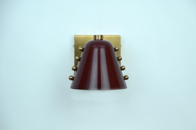 This Handcrafted Wall Light Pairs a Rich Wine Cone Shade with Warm Brass Detailing, Showing a Clean Silhouette and Carefully Placed Rivets that Add Texture without Overpowering the Simple Design, Frost Lights.
