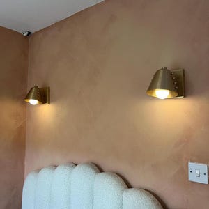 A Decorative Wine Colored Cone Wall Lamp with Handcrafted Brass Construction, Photographed to Highlight Its Compact Proportions, Tapered Shade, and Distinctive Rivet Details in A Mid Century Inspired Form, Frost Lights.